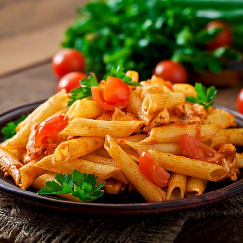 Penne pasta in tomato sauce with chicken and tomatoes  on a wooden table